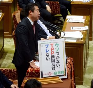 自民党のポスター「TPP断固反対」を示しながら質問に立つ同僚議員の福島伸享さん。